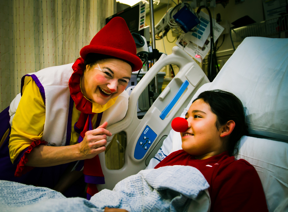 Victoria Millard as Dr. La Fou does a "red nose transplant" on a smiling child in a hospital bed